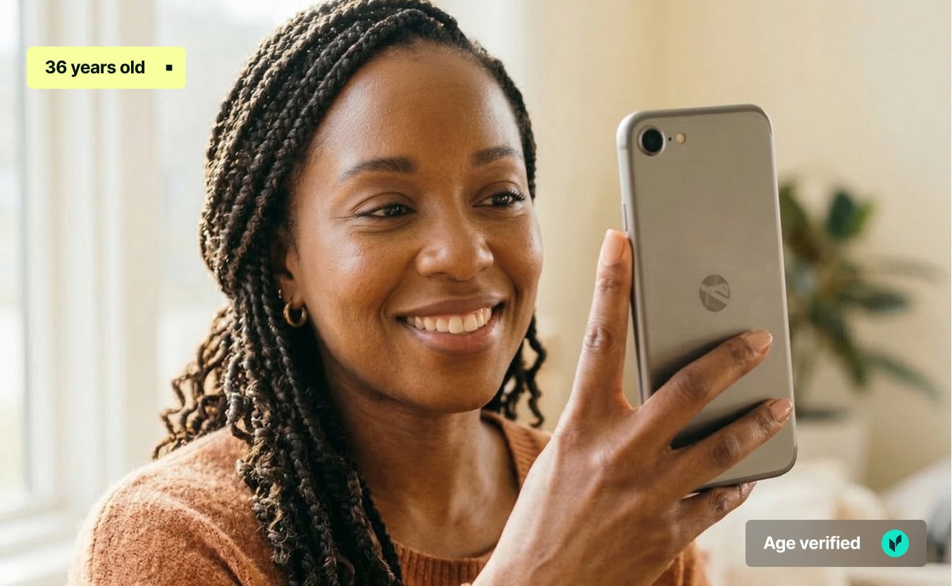 A smiling woman with braided hair holding up a smartphone to her face, as if undergoing a facial verification scan. The image features two digital graphic overlays: a yellow badge in the top-left corner reading 